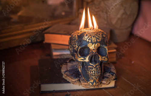 Maya carved skull candle with burning flames on old spell book, pagan ritual altar and esoteric concept 