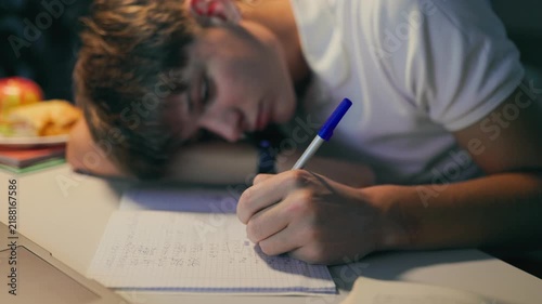 Exhausted youth sleeping on his notebook while doing academic homework.