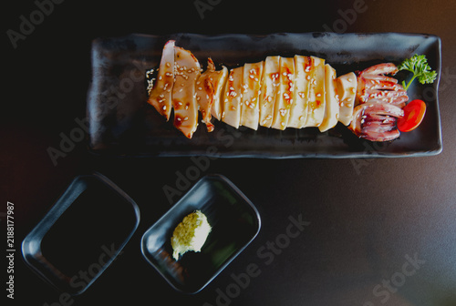 Grilled squid with teriyaki sauce and sesame seeds served with wasabi on a black plate.