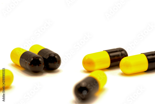Yellow and black capsule pills scattered on a white background.