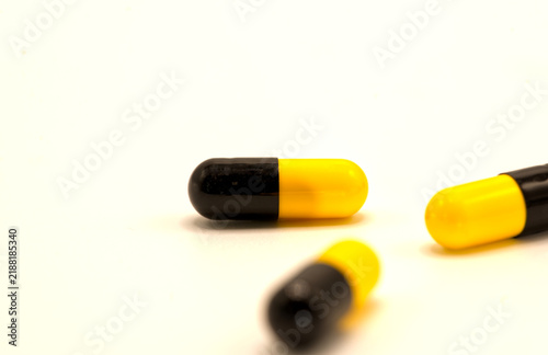 Yellow and black capsule pills scattered on a white background.