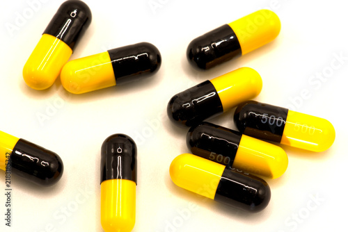 Yellow and black capsule pills scattered on a white background.