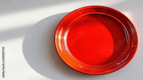 Bright red ceramic plate resting on a white surface with strong morning sunlight and shadows