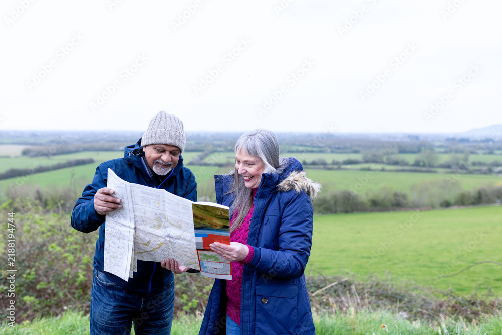 Obraz premium Smiling elderly white man and woman reading a map outdoors in countryside