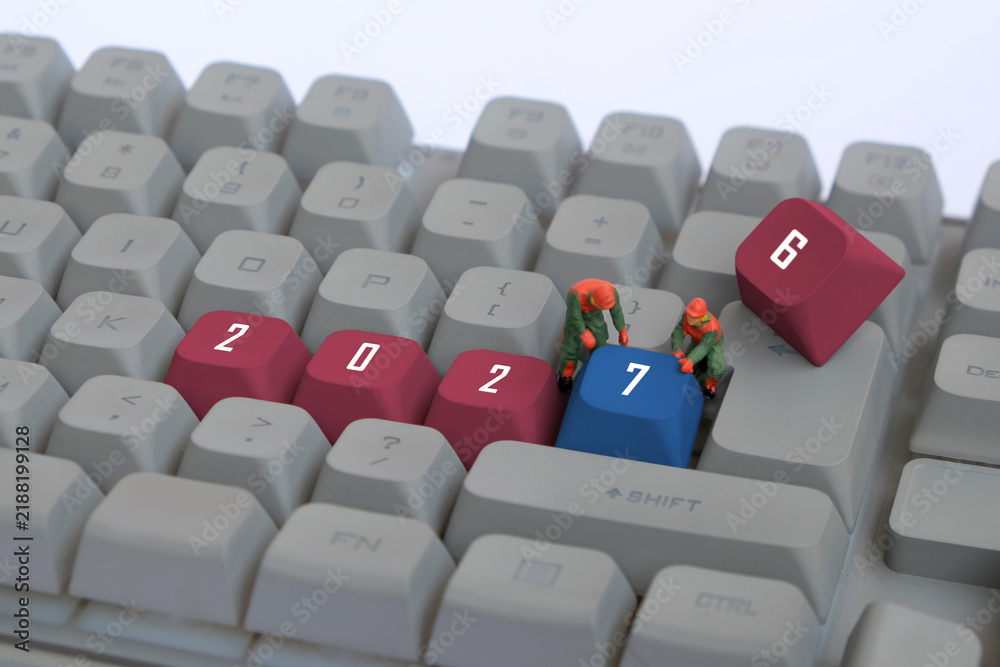 Obraz premium Miniature workers changing 2026 to 2027 on computer keyboard with red and blue keycaps