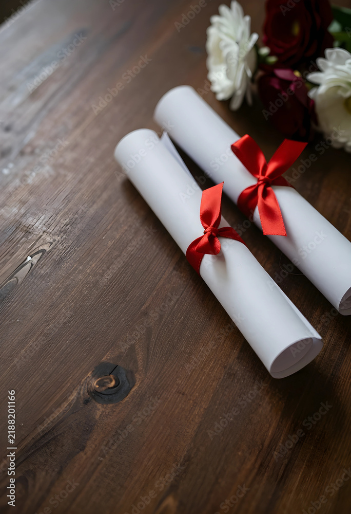 Obraz premium Graduation and academic achievement, two rolled diplomas with red ribbons on a rustic wooden table with flowers for celebration and success ceremony