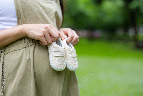 Obraz na plátně Pregnant woman holding tiny baby shoes in a green park