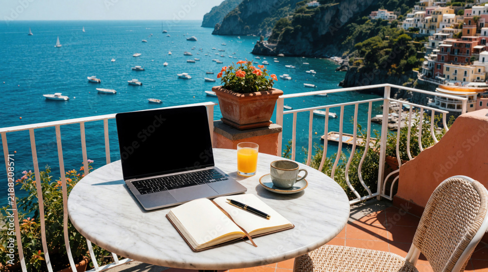 Obraz premium Laptop and notebook sit on a marble table on a seaside balcony with Mediterranean town backdrop. Orange juice and coffee await next to open planner, pen, and laptop.