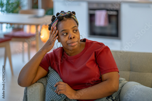 Canvastavla Thoughtful black woman sits at home with hand against head, looking away while feeling stressed, mentally tired