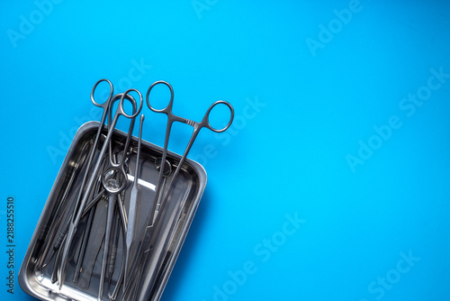 Sterile surgical instruments and tools - scalpels, scissors and others - in a stainless tray on blue background, top view