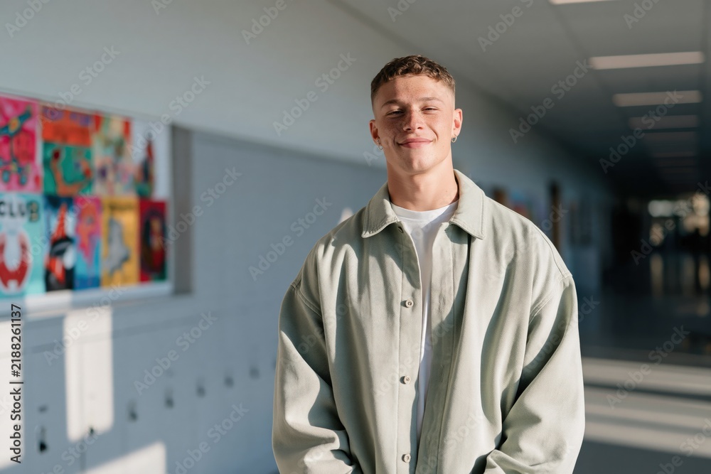 Obraz premium Young smiling male student portrait in school hallway with lockers and colorful artwork for background and banner design