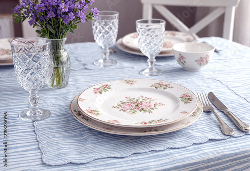 Elegant table setting with floral china crystal glasses and fresh flowers on striped tablecloth