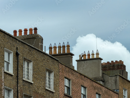 Bild auf Leinwand Rows of terracotta chimney pots rise above historic brick townhouses beneath a dramatic cloudy sky in Dublin, Ireland