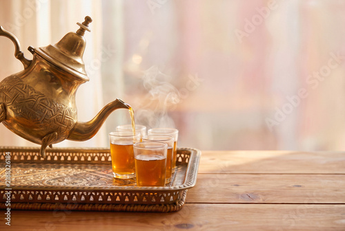 Brass teapot pouring hot tea into glasses on ornate tray