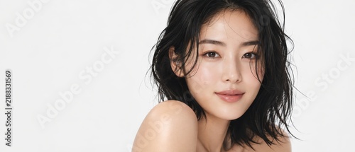 young asian woman with wet look wavy black hair and dewy skin looking directly at the camera against a white studio background