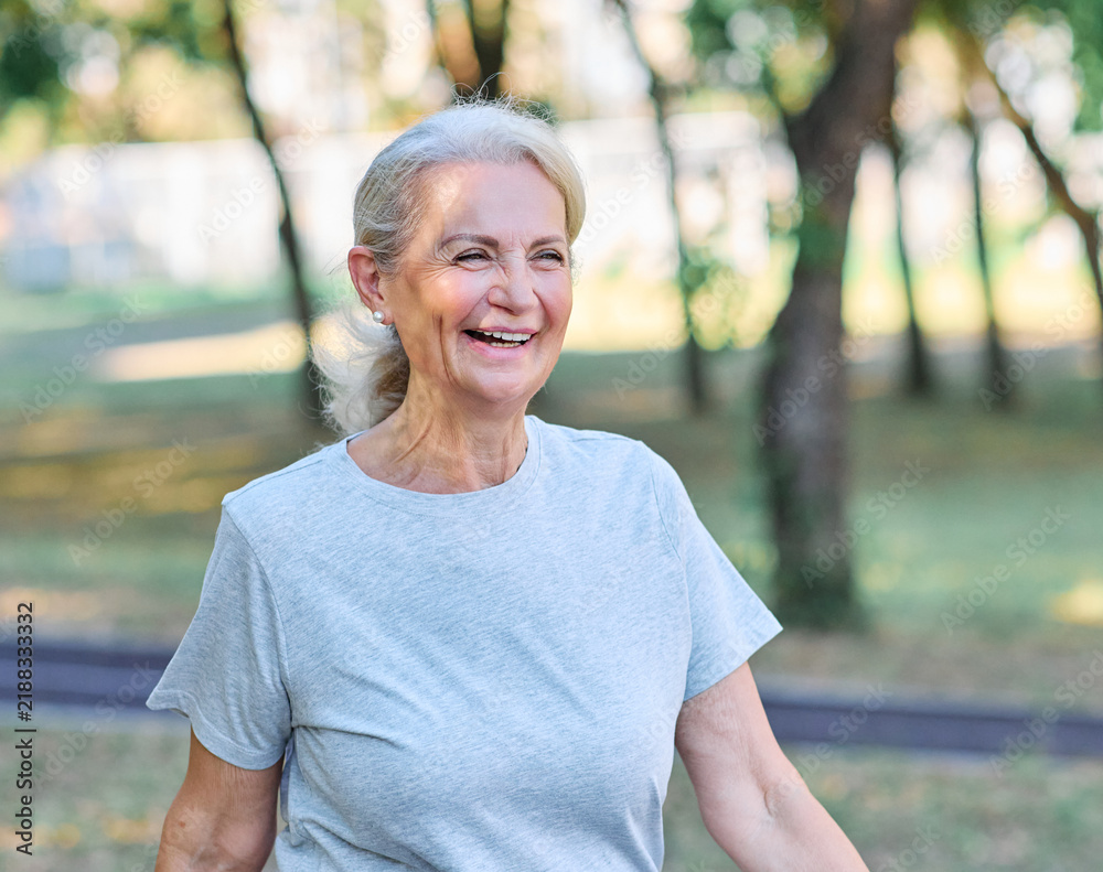 Fototapeta premium Smiling active mature elderly woman jogging running or speed walking in the park