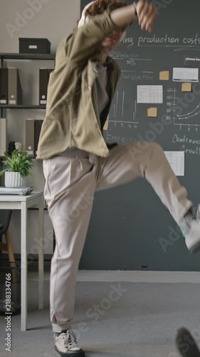 Vertical video of cheerful Caucasian young adult man wearing headphones dancing happily in modern office. Footage suited for workplace wellness campaigns and music streaming ads
