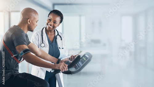 Female doctor monitoring patient on exercise bicycle during cardiac stress test background banner