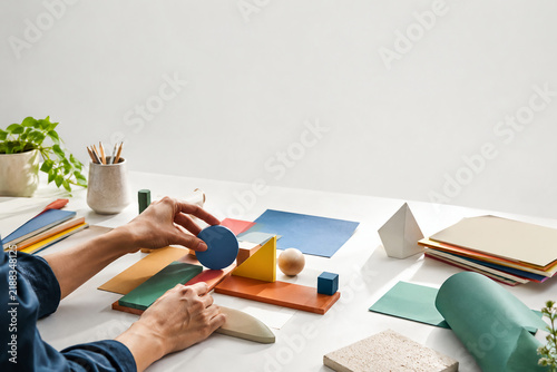 designer working with colorful geometric shapes and material samples on white table