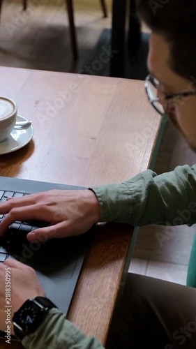 Vertical video. Top view of man in casual clothes is typing on a laptop, sitting at a table. Student is studying in cafe at table with coffee cup. People and technology concept.