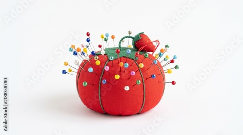 Red tomato pincushion with colorful pins isolated on white background for sewing and crafting