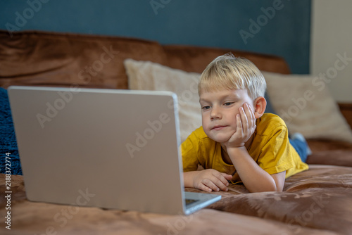 Obraz na płótnie Bored small boy lies on sofa watching laptop with tired eyes, low interest during prolonged screen time at home