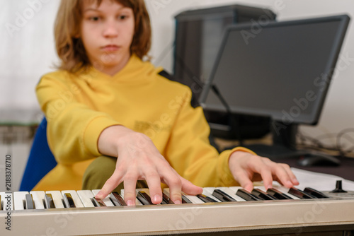 Принти на полотні Concentrated teenager boy playing electronic piano at home A closer view emphasizes both hands on the keys as the teenager practices at the electronic instrument beside the computer monitor