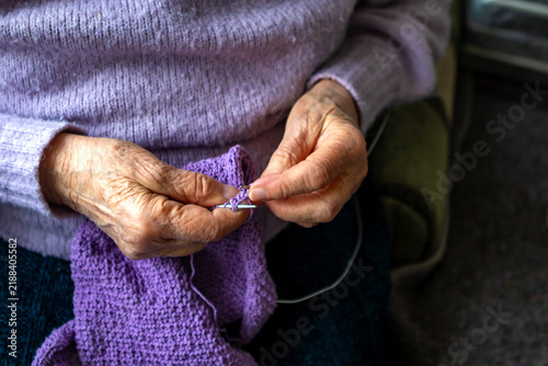 Konstfotografi Elderly hands knitting purple yarn by a window, calm hobby and handmade comfort