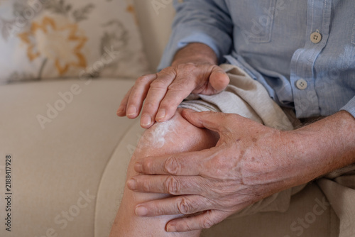 Senior adult applying pain relief cream to knee, managing joint discomfort and arthritis symptoms, finding comfort with topical medication