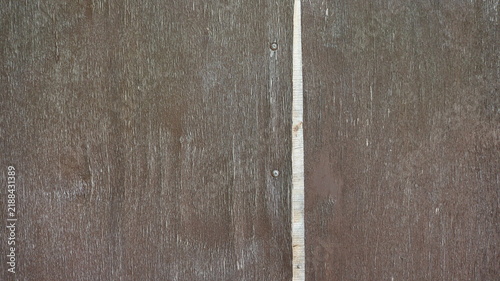 An old brown wooden surface with a pronounced texture. A vertical light-colored gap runs down the center, and two metal self-tapping screws are visible to its left.