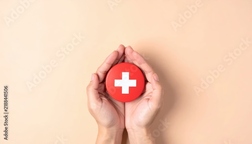 Hands holding a red circle with a white medical cross symbol for health insurance and care.