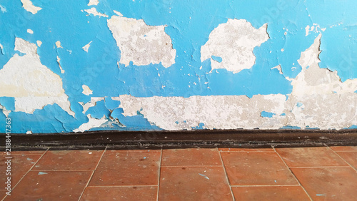 Peeling off blue paint on old wall. tiled floor. Grunge cracked concrete weathered rustic surface. Distressed interior room background vintage loft design. Poverty. Peel wallpaper. Texture.