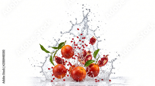 Pomegranate fruit and water droplet splash with green leaf and red seed arrangement creating fresh motion on white background
