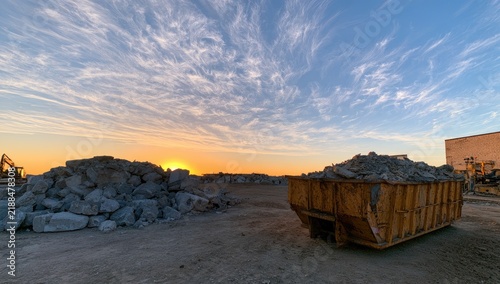 Naklejka Debris-filled dumpster and rubble pile under a dramatic sunset sky