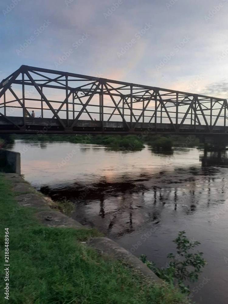 Fototapeta premium Old iron bridge over a rural river at sunset 