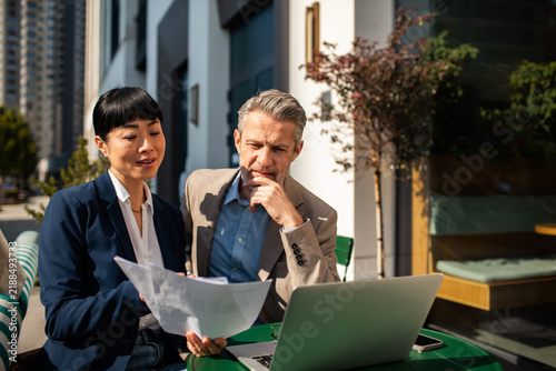 Two business professionals reviewing documents at outdoor cafe