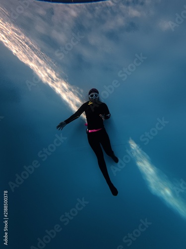 Freediver floating in blue pool water with natural sunlight refraction beam