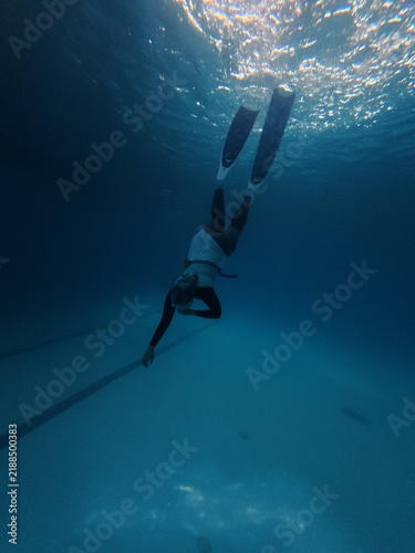 Freediver diving down deep blue pool wearing long fins and wetsuit