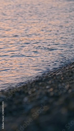 Pebble shore with gentle waves and orange reflections