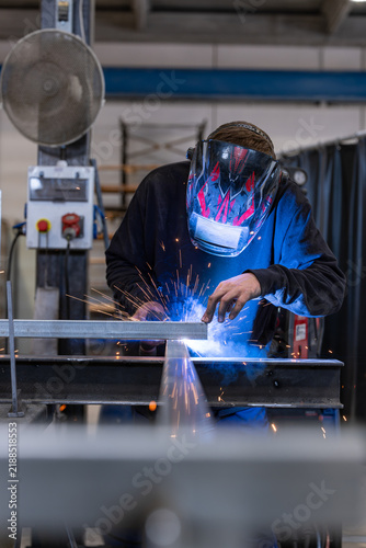 Bild auf Leinwand Welder in a mask welding a steel bar with bright sparks