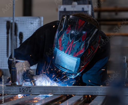 Obraz na plátně Welder bent over a steel frame with sparks flying