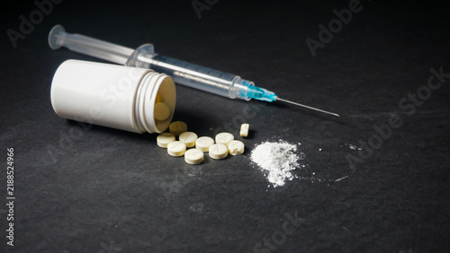 Foto One disposable medical syringe in three mililiter size, white powder and several pills spilled from white bottle