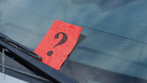 Bild auf Leinwand A crumpled red paper note with a black question mark is placed under a windshield wiper of a car, representing a mystery message or an unexpected notification