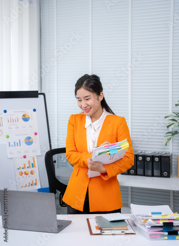 Foto Successful Presentation: A focused businesswoman delivers a compelling presentation, confidently holding a stack of documents beside a flip chart filled with insightful charts and graphs