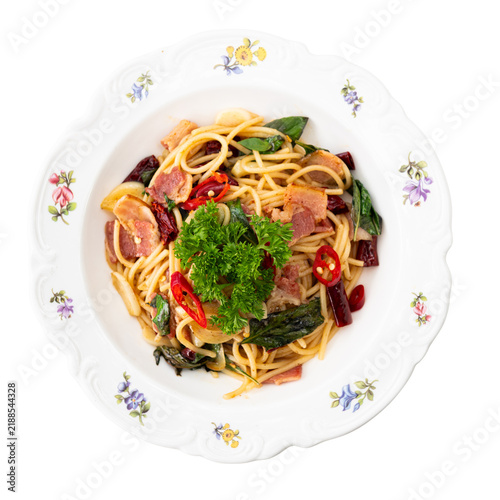 Top view of spicy spaghetti with bacon, red chili, garlic, basil and fresh parsley served on a floral ceramic plate, savory fusion pasta meal isolated cutout object,