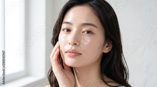 Young woman touching her face with glowing skin after applying daily facial skincare