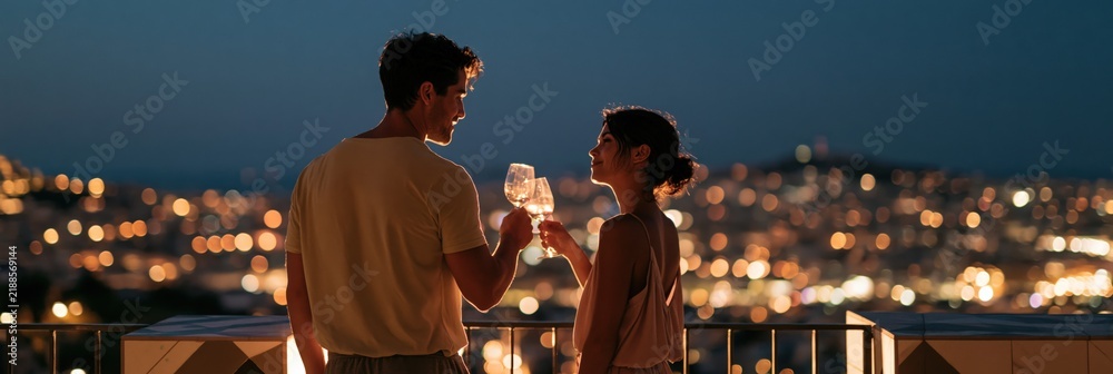 Obraz premium Romantic couple toasting with wine glasses on balcony at night overlooking city lights for anniversary banner and romance background design