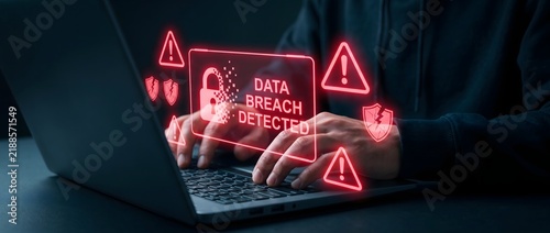 Data breach detected warning screen on laptop with hacker typing fast.