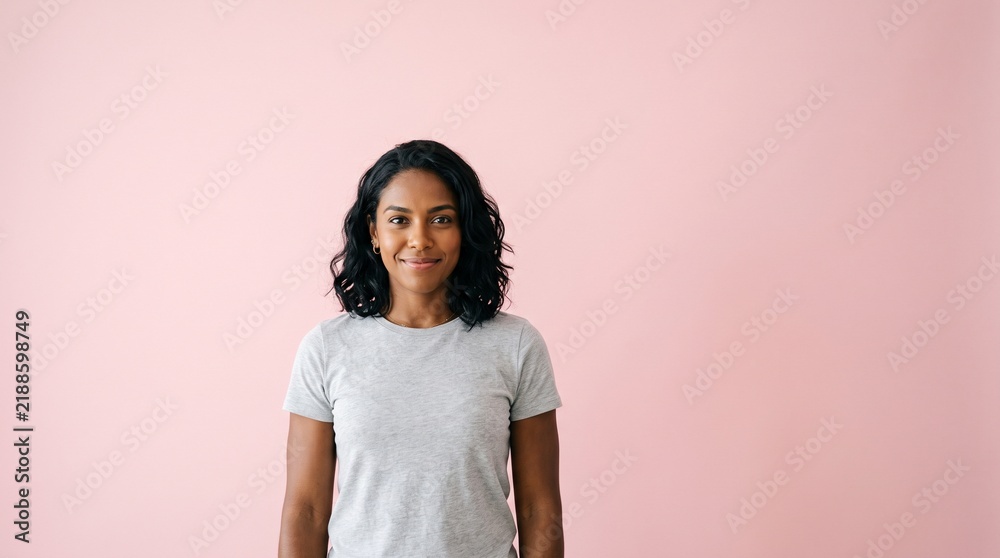 Obraz premium A smiling young woman with dark wavy hair wearing a grey t-shirt against a soft pink background