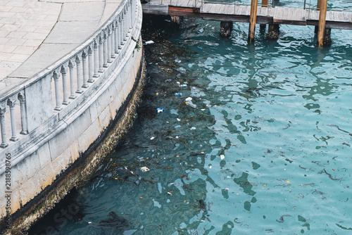 Fotografie Plastic waste floating in a Venetian canal beside marble balustrade